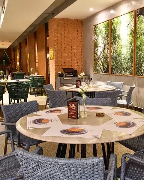 Varanda com mesas redondas, cadeiras de fibra e painéis de vegetação